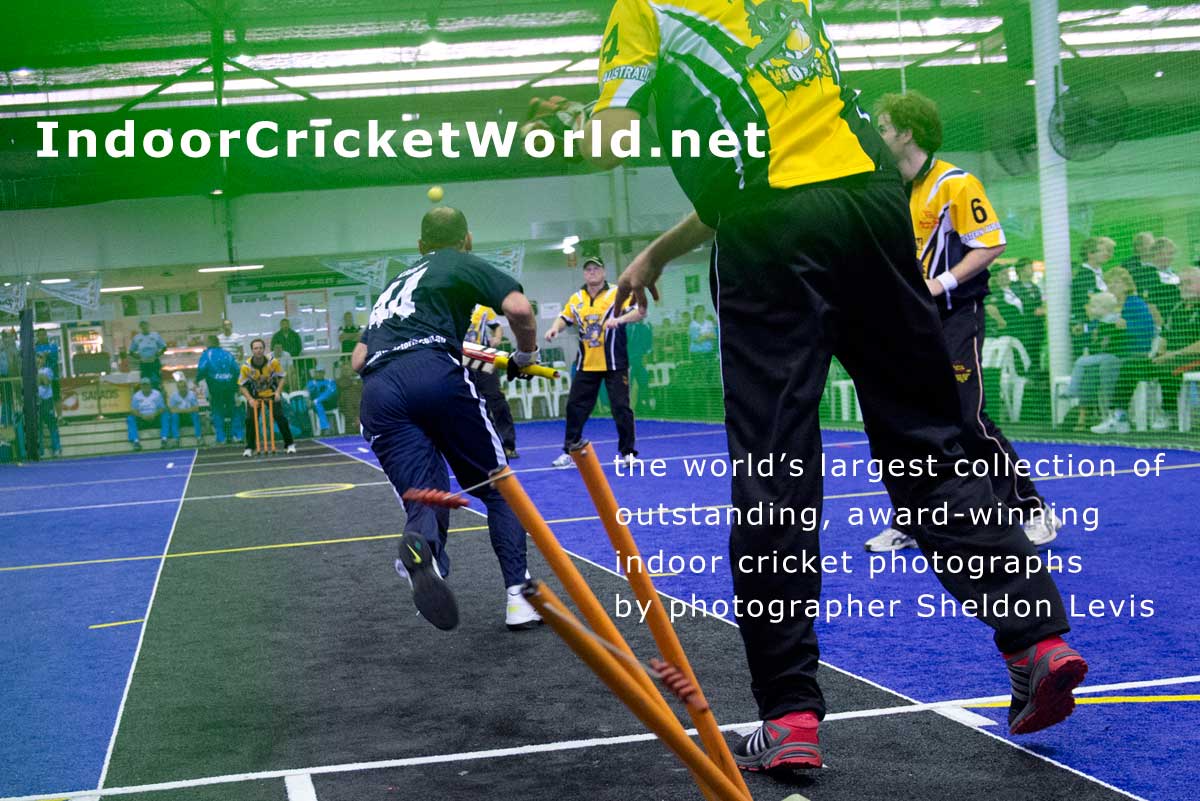 close up of indoor cricket wicket-keeper throwing to bowler's end to run out batsman, stumps scattered, batsman scrambling to other end, ball in flight