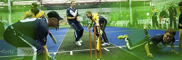 Indoor Cricket Batsman holding his crease as non-striker reaches same end, with fielders scrambling to field ball after call of 'third ball'